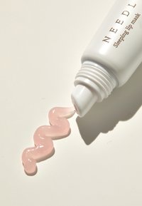 Tubo bianco di maschera per labbra con prodotto rosa brillante e morbido che fuoriesce a zigzag su una superficie chiara. Il testo recita "NEEDL Sleeping Lip Mask."
