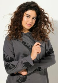 Felpa grigia con stampa di farfalle nere, in tessuto morbido, maniche lunghe e cappuccio con cordino. Il design include un motivo testurizzato.