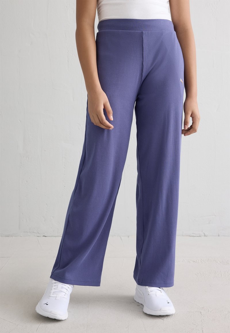 Μωβ φαρδιές παντελόνες με ριμπ ύφανση και ψηλή λογότυπη ζώνη, που συνοδεύονται από λευκά αθλητικά παπούτσια.