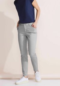 Jasnoszare spodnie typu slim fit o gładkiej fakturze, pięć kieszeni i zapięcie na guzik, w połączeniu z białymi sneakersami i granatową górą.