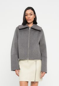 Γκρι κοντό μπουφάν με φαρδιά ριμπ ύφανση στο γιακά, κλείσιμο με φερμουάρ μπροστά και φαρδιά μανίκια, συνδυασμένο με κρέμ δερμάτινη φούστα.