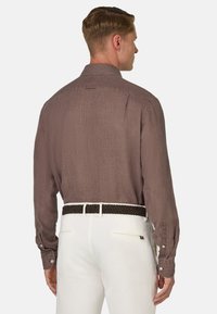Camicia marrone a maniche lunghe con tessuto strutturato, vestibilità slim, polsini abbottonati, indossata con pantaloni avorio e una cintura nera intrecciata.