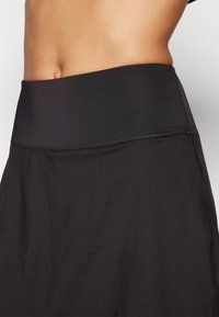 Jupe de sport noire avec une taille haute, texture lisse et détails de couture visibles le long des coutures.