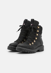 Botas de tobillo de cuero negro con herrajes dorados, acabado texturizado, diseño de cordones y suela de goma gruesa. Incluye acentos cosidos.
