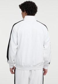 Witte zip-up jas met zwarte zijstrips, met een hoge kraag en ribgebreide manchetten. Gemaakt van glad, rekbaar materiaal.