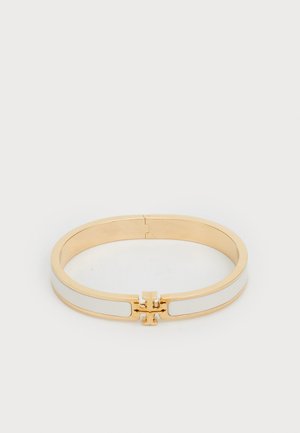 Kultainen bangle-rannekoru, jossa on valkoiset emaliviilut, sileät reunat ja solkilukko. Yksinkertainen, pyöreä muotoilu ilman koristeita.