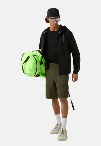 Sort zip-up hoodie, sort skjorte, grøn duffelbag, olivenfarvede shorts, hvide sokker, grå sneakers og spejlede solbriller.