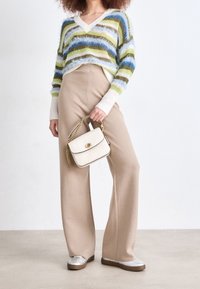 Suéter tejido con rayas multicolores, pantalones beige de pierna ancha y un bolso crema con detalles de cadena dorada; se pueden ver materiales texturizados.