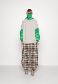 Strickpullover in Hellgrau mit grünen strukturierten Ärmeln und einem hohen Kragen, kombiniert mit weit geschnittenen gestreiften Hosen in bunten Mustern.
