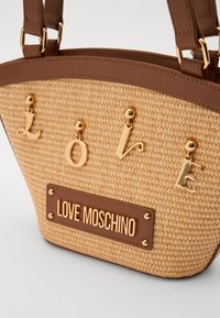 Kudottu olkainlaukku, jossa on ruskeita keinonahkaosia. Varustettu kultaisilla "LOVE"-kirjaimilla ja kullalla varustetulla plaketilla, jossa on teksti "LOVE MOSCHINO".