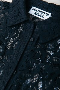 Camicia in pizzo nero con intricati motivi floreali, un colletto e bottoni neri, con un'etichetta che reca la scritta "COLOURFUL REBEL."