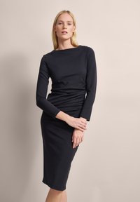 Figurbetontes schwarzes Kleid mit langen Ärmeln, Rundhalsausschnitt, gerafftem Detail an der Taille, glatter Textur und kniefreiem Schnitt.