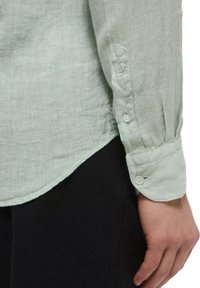 Camicia in lino verde chiaro con maniche lunghe, polsini con bottoni e orlo curvo. Tessuto morbido, design casual e dettagli minimi.