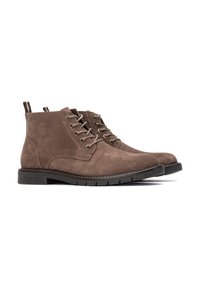 Botas de tobillo de ante marrón con diseño de cordones, punta redonda, suela de goma y tirador contrastante en la parte trasera. La superficie texturizada añade detalle.
