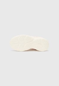 Semelle de chaussure blanche avec un motif de crampons triangulaires détaillé, vue par le dessous sur un fond clair.