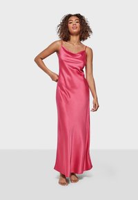Pink satin maxi dress with a cowl neckline, adjustable spaghetti straps, and a smooth, full-length silhouette. Model is barefoot.