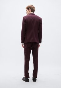 Μπορντό κοστούμι με εφαρμοστή γραμμή, μονό σκίσιμο και μακριά μανίκια. Μαύρα παπούτσια ολοκληρώνουν την εμφάνιση. Απλές, καθαρές γραμμές.