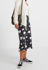 Blommig midikjol med marinblå och vita ränder, prydd med ett mönster av vita rosor. Kombinerad med en krämfärgad skjorta med knappar och svarta sneakers.