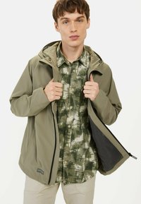 Leichte, olivgrüne Jacke mit Kapuze, Reißverschluss vorne und Mesh-Futter, getragen über einem strukturierten, dunkelgrünen gemusterten Hemd.
