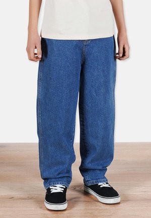Wide-leg blue denim jeans with visible stitching, a high waist, and a relaxed fit, paired with black sneakers and a light-colored top.