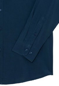 Camicia a maniche lunghe blu navy con una texture liscia, chiusura frontale con bottoni, polsini con un solo bottone e orlo curvo. Cuciture visibili e bottoni coordinati.