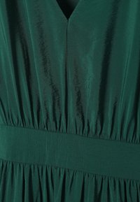 Robe en satin vert profond avec décolleté en V, taille froncée et texture de tissu lisse légèrement réfléchissante.