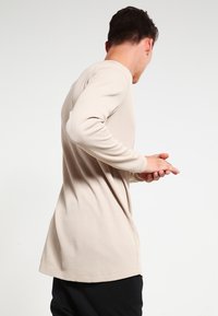 Långärmad beige ribbad topp med rund krage, har en avslappnad passform och något böjd nederkant, bärs med svarta byxor.