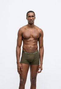 Πράσινα βαμβακερά μποξεράκια με λογότυπο στη μέση με κόκκινες, λευκές και μπλε λεπτομέρειες. Το μοντέλο στέκεται μπροστά σε ένα απλό λευκό φόντο.