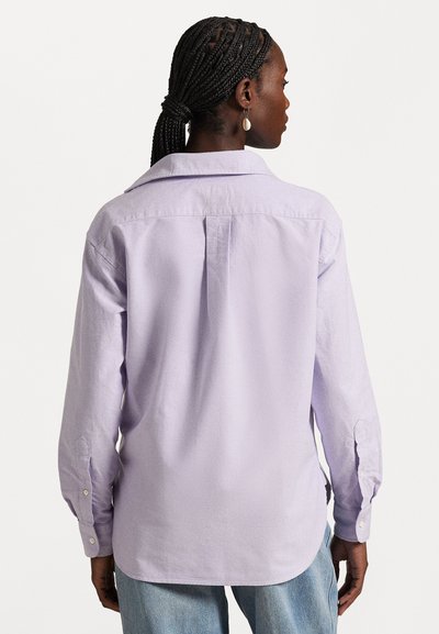 Lavender button-up shirt with a relaxed fit, long sleeves, single back pleat, and curved hem. Features white buttons on the cuffs.