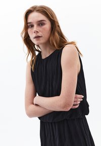 Schwarzes ärmelloses Kleid mit strukturiertem, plissiertem Design. Rundhalsausschnitt und eine lockere Passform, die den glatten Stoff und den subtilen Glanz zur Geltung bringt.