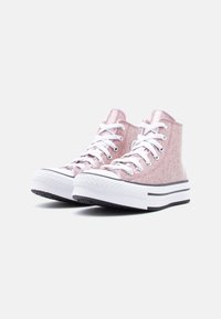 Ζευγάρι ροζ παπουτσιών υψηλού επάνω μέρους με γκλίτερ, λευκά κορδόνια και χοντρές λευκές σόλες σε απλό ανοιχτό φόντο.