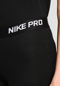 Leggings neri con un ampio elastico in vita che presenta la scritta "NIKE PRO" in lettere bianche. Texture liscia, design aderente, adatti per l'abbigliamento sportivo.