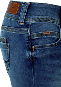 Close-up of blue denim jeans showing back pocket, belt loop, stitching details, and brown leather brand tags reading "Pepe Jeans."