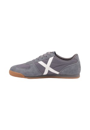 Zapatilla gris de ante con diseño en forma de X blanca cosida en el lateral y suela de goma marrón, vista desde el lado exterior.
