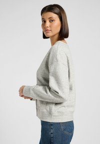 Ljusgrå sweatshirt med en strukturerad tyg, sänkta axlar, ribbade ärmslut och nederkant. Kombinerad med mörkblå jeans.