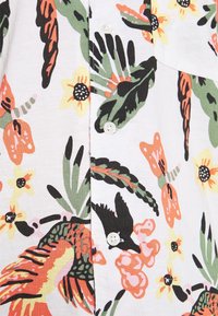 Chemise à manches courtes à motif floral avec des feuilles et des fleurs colorées sur fond blanc, dotée de boutons blancs et d'un détail de poche.