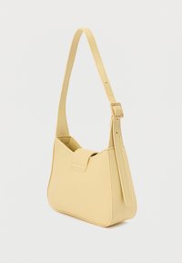 Μικρή ωχρή κίτρινη τσάντα ώμου με έναν ρυθμιζόμενο λουρί και κλείσιμο με καπάκι, εμφανίζεται πάνω σε απλό λευκό φόντο.