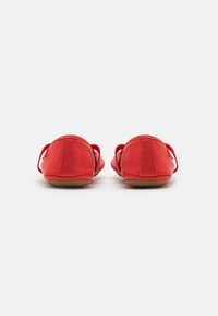 Zapatos planos de cuero rojo con una textura suave, puntera redondeada y correas de tela a los lados para un ajuste seguro. La suela es marrón y plana.