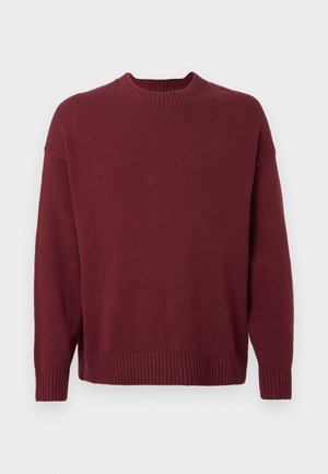 Vīna sarkana adīta džempera ar ribotu apaļu apkakli, garām piedurknēm un ribotu apakšu. Gluda tekstūra bez rakstiem vai rotājumiem.