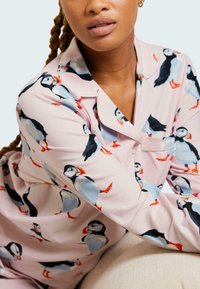 Ljust rosa pyjamaströja med ett upprepat puffin-mönster. Tyget är mjukt, lättviktigt och har en klassisk krage och knappdetaljer.