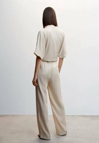 Ensemble en maille beige comprenant un haut à manches courtes et une coupe ample, associé à un pantalon à jambes larges, mettant en valeur une texture douce et un design minimaliste.