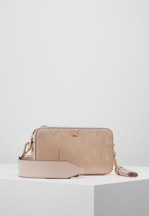 Beżowa torba na ramię z geometrycznym wzorem, złotym logo MK, szerokim paskiem i frędzlowym dodatkiem, ustawiona na białym postumencie na gładkim tle.