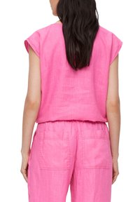Roze linnen top met kapmouwen, relaxte pasvorm en een elastische tailleband aan de achterkant; gedragen met bijpassende losvallende broek met twee achterzakken.