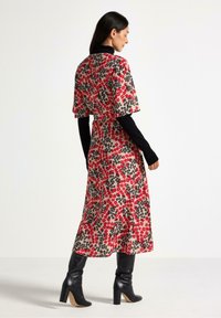 Abito floreale avvolgente in rosso, nero e beige. Maniche corte, vita sagomata, gonna svasata. Abbinato a stivali neri con tacco al ginocchio.