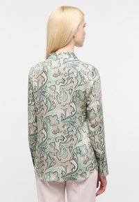 Langærmet bluse med et blomster- og ornamentmønster i grøn, beige og sort. Glat stof med en let glans og kravedetalje.