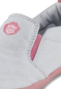 Gray canvas shoe with pink accents, featuring a stitched design and a round logo patch on the upper. The sole is a soft pink rubber.