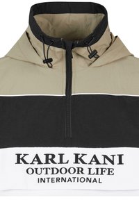 Pulóver s krátkym zipsom v béžovej, čiernej a bielej farbe. Má vysoký golier, nastaviteľné šnúrky a potlačený logotyp vpredu.