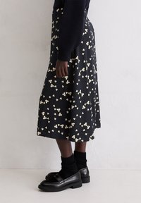 Schwarzer Midirock mit einem Blumenmuster in Creme. Der Stoff hat eine glatte Textur, ein fließendes Design und eine ausgestellte Silhouette.