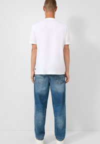 Witte ronde hals t-shirt gecombineerd met grote blauwe spijkerbroeken. De spijkerbroeken hebben een vervaagde afwerking en zichtbare achterzakken.