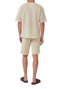 Lichtbeige korte mouw top en shorts gemaakt van een gestructureerde, ademende stof met een ruitpatroon en een klein label aan de achterkant.